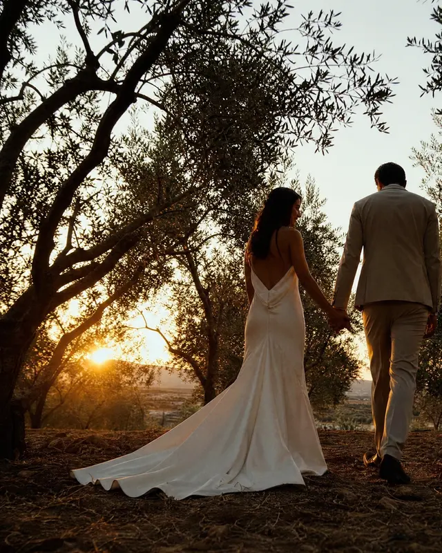 The bride and groom walking among olive trees at sunset
