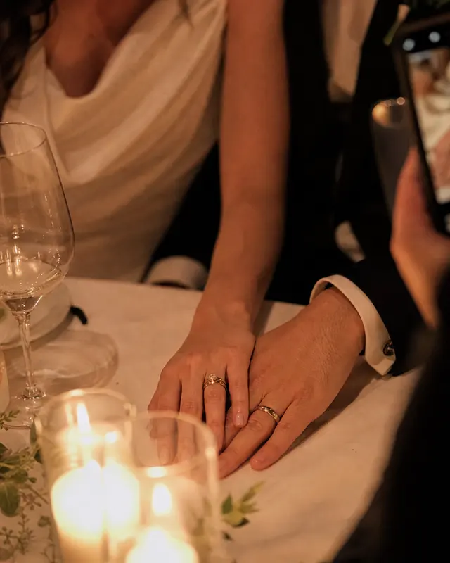 The couple's hands and wedding rings on a candlelit table