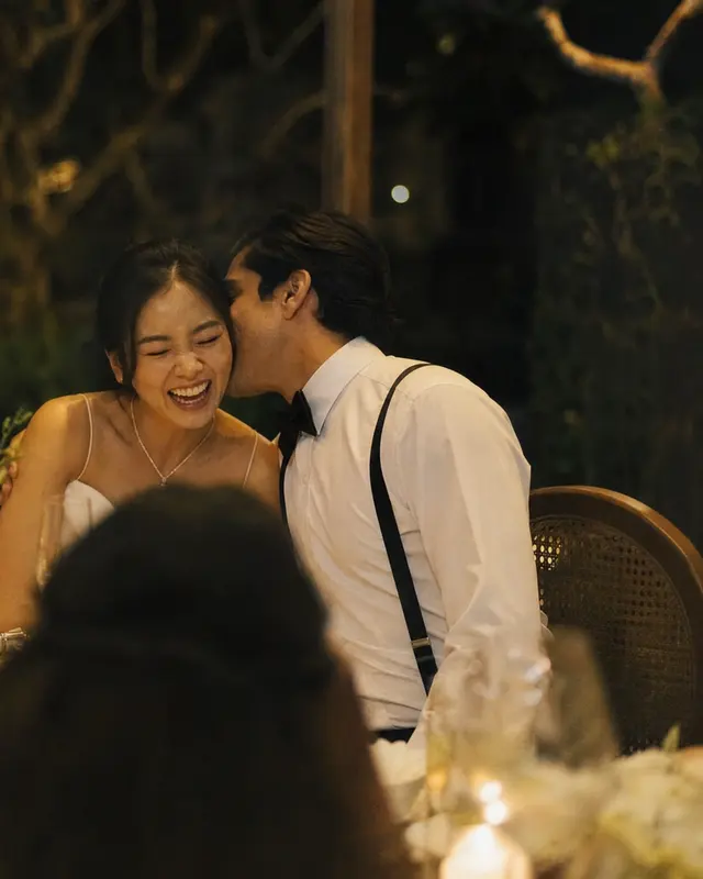 The groom kissing the laughing bride's cheek at a table with calla lilies